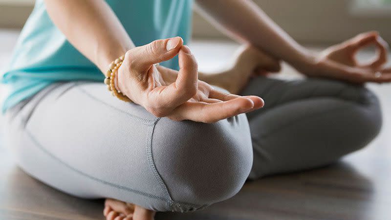 photo of the lower half of a person sitting cross-legged on the floor with their fingers in a mudra on their knees