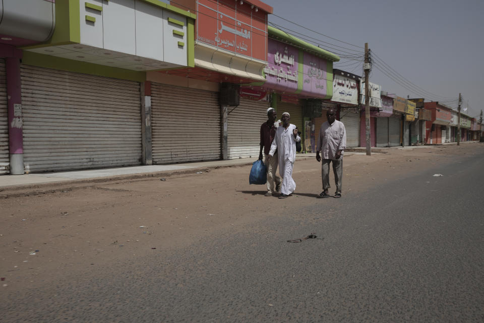 People walk past shuttered shops in Khartoum, Sudan, Monday, April 17, 2023. Sudan's embattled capital has awoken to a third day of heavy fighting between the army and a powerful rival force for control of the country. Airstrikes and shelling intensified on Monday in parts of Khartoum and the adjoining city of Omdurman. (AP Photo/Marwan Ali)