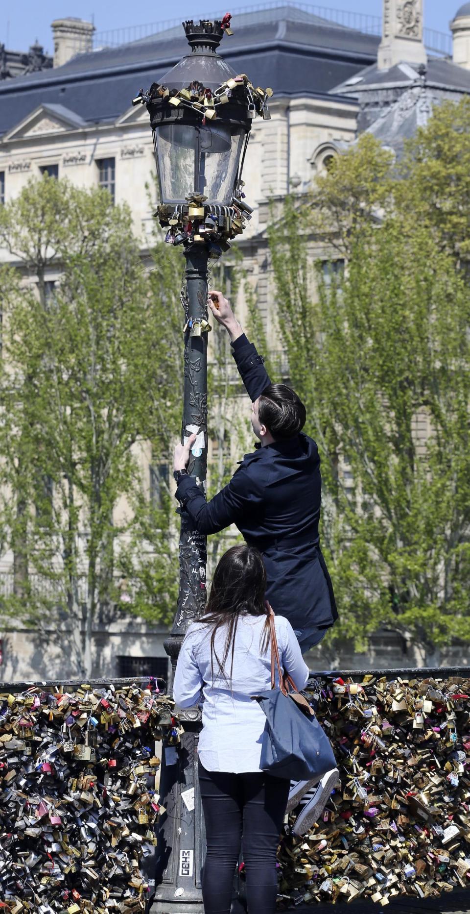 A man tries to fix a love lock on a street lamp on the Pont des Arts in Paris, Wednesday April 16, 2014. A recent fad among travellers of hitching padlocks on bridges and at tourist attractions worldwide to symbolically immortalize their amorous attraction has swept up this reputed City of Love more than most. Now, two American-born women who live in Paris say they've had enough, launching a petition drive to try to get mostly laissez-faire city officials to step in and do something about what they call an unbearable eyesore in a majestic municipality. (AP Photo/Remy de la Mauviniere)