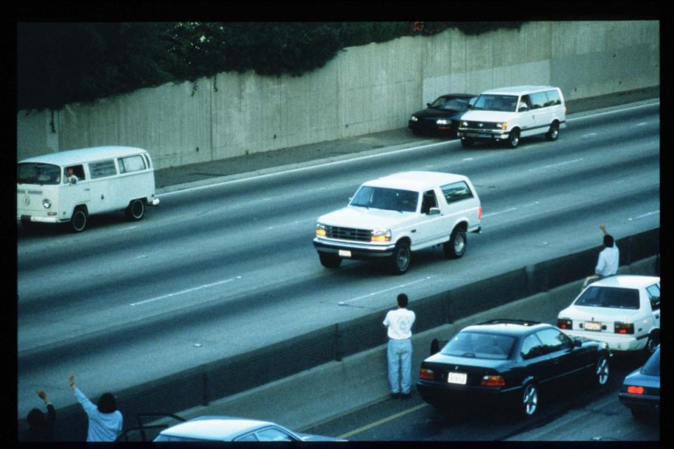 Motorists wave as police cars pursue the Ford Bronco (white, R) driven by Al Cowlings, carrying fugitive murder suspect O.J. Simpson, on a 90-minute slow-speed car chase June 17, 1994 (Getty)