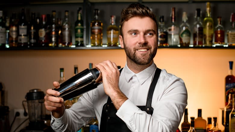 smiling male bartender shaking cocktail