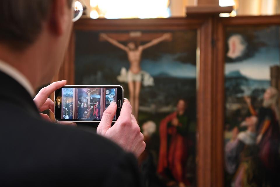 A man takes a picture of "Triptych of the Crucifixion," which is attributed to Flemish painter Joachim Patinir.