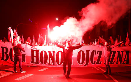 People carry Polish flags and burn flares during a march marking the 100th anniversary of Polish independence in Warsaw, Poland November 11, 2018. The banner reads "God, Honour, Fatherland". REUTERS/Kacper Pempel