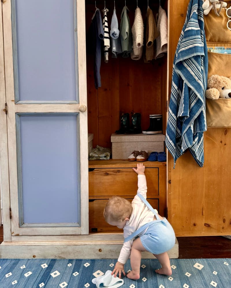 Baby hanging on to armoire.