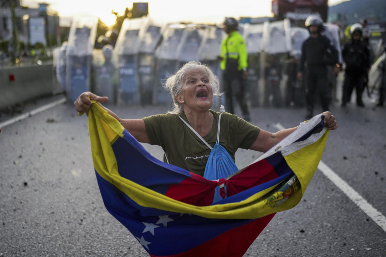 Consuelo Marquez holds a Venezuelan flag in front of police blocking demonstrations against the official election results declaring President Nicolas Maduro's reelection, the day after the vote in Caracas, Venezuela, Monday, July 29, 2024. (AP Photo/Matias Delacroix)