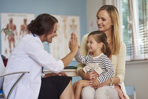 A female doctor high-fiving a child sitting on her mother's lap.