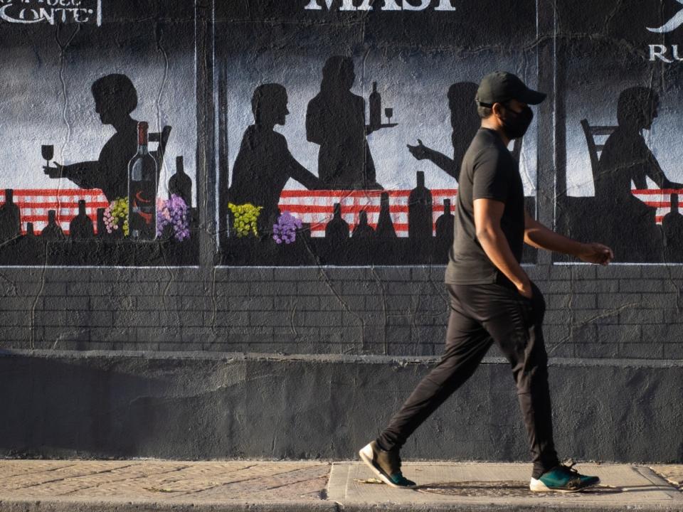 A pedestrian in a mask walks past a mural adorning the side of a restaurant in Ottawa's Little Italy neighbourhood on Oct. 22, 2021. (Trevor Pritchard/CBC - image credit)