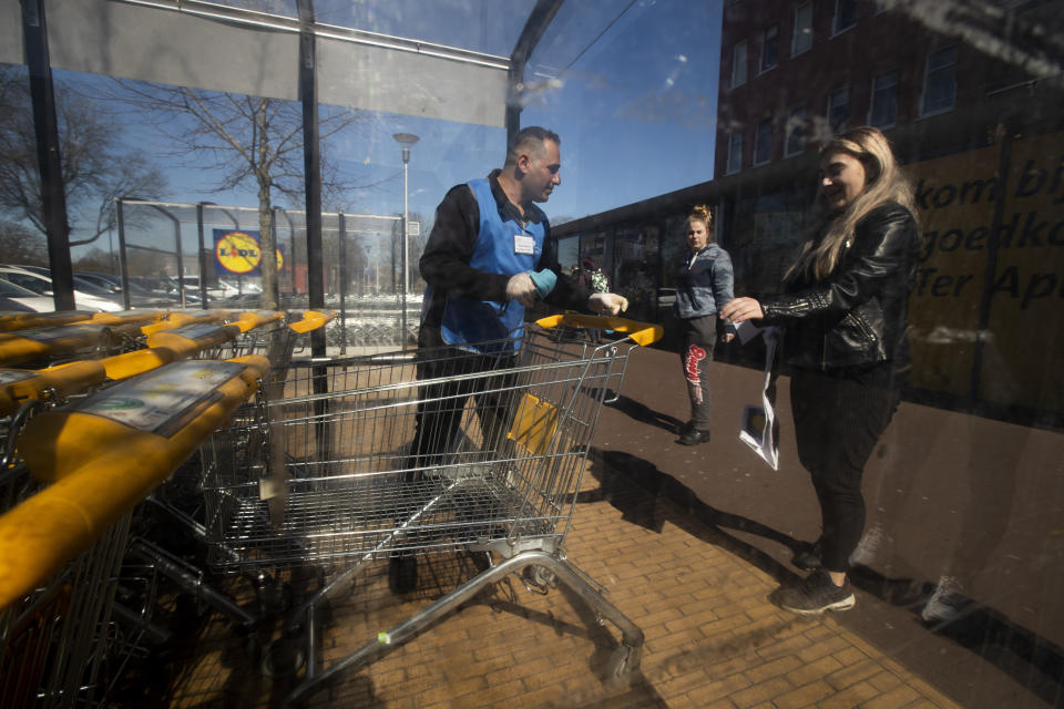 Raffat Altekrete, left, is battling the coronavirus one shopping cart at a time as he uses a disinfecting spray outside a supermarket in Ter Apel, north-eastern Netherlands, Tuesday, March 31, 2020. The Iraqi migrant, armed with latex gloves, a cleaning rag and a spray bottle of disinfectant is also aiming to express his gratitude and win hearts in a small Dutch community that hosts the Netherlands' biggest asylum seeker center. (AP Photo/Peter Dejong)