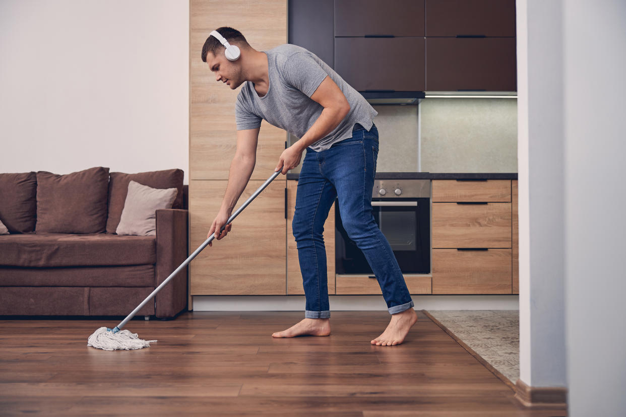Attractive brunette man with mopping stick washing floor while listening to music in headphones