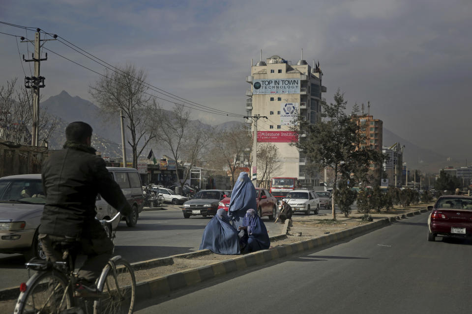 Afghan women sit on a road divider as they seek alms from pedestrians outside a camp for internally displaced people in Kabul, Afghanistan, Monday, Dec. 9, 2019. Tens of thousands of internally displaced Afghans live in camps, which lack basic facilities, across Afghanistan. (AP Photo/Altaf Qadri)
