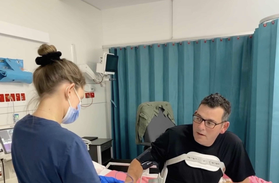 Daniel Andrews pictured sitting up in his hospital bed with a nurse after his fall on the Mornington Peninsula.