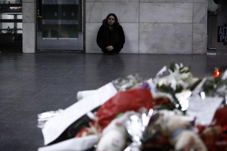 A young woman sits near flowers and candles, in memory of the victims of the trains' collision, at the train station in the port city of Thessaloniki, northern Greece, Thursday, March 2, 2023. Emergency crews inched through the mangled remains of passenger carriages in their search for the dead from Tuesday night's head-on collision, which has left dozens passengers dead in Greece's worst recorded rail accident. (AP Photo/Giannis Papanikos)