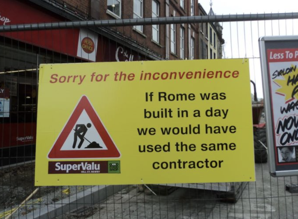 Street construction sign on a gate: "Sorry for the inconvenience: If Rome was built in a day we would have used the same contractor"