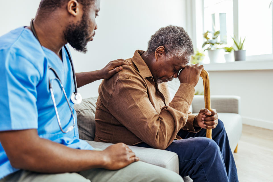 A medical staff member comforts an older African American man. (Getty Images)