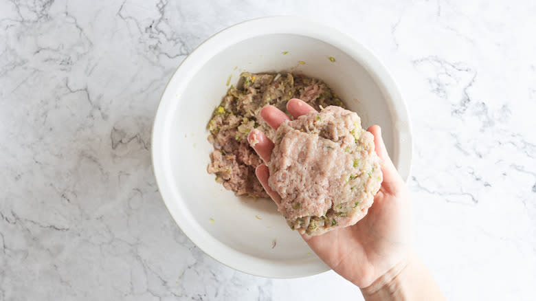 Hand holding shaped burger patty above ground burger mix in bowl 