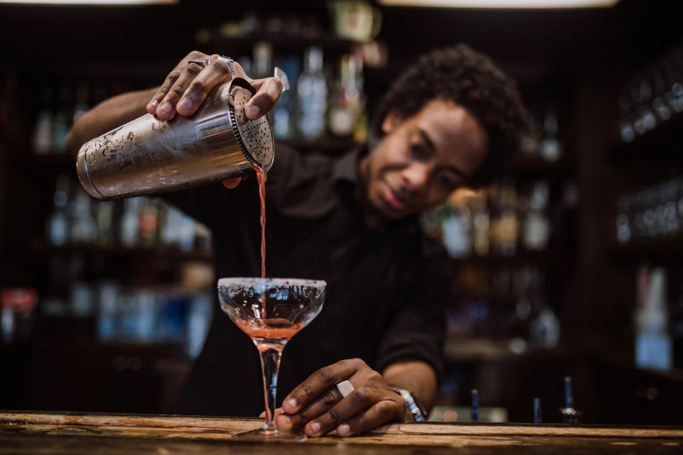 Bartender focusing on pouring a cocktail from a shaker into a glass on a bar counter, creating a vibrant and inviting atmosphere