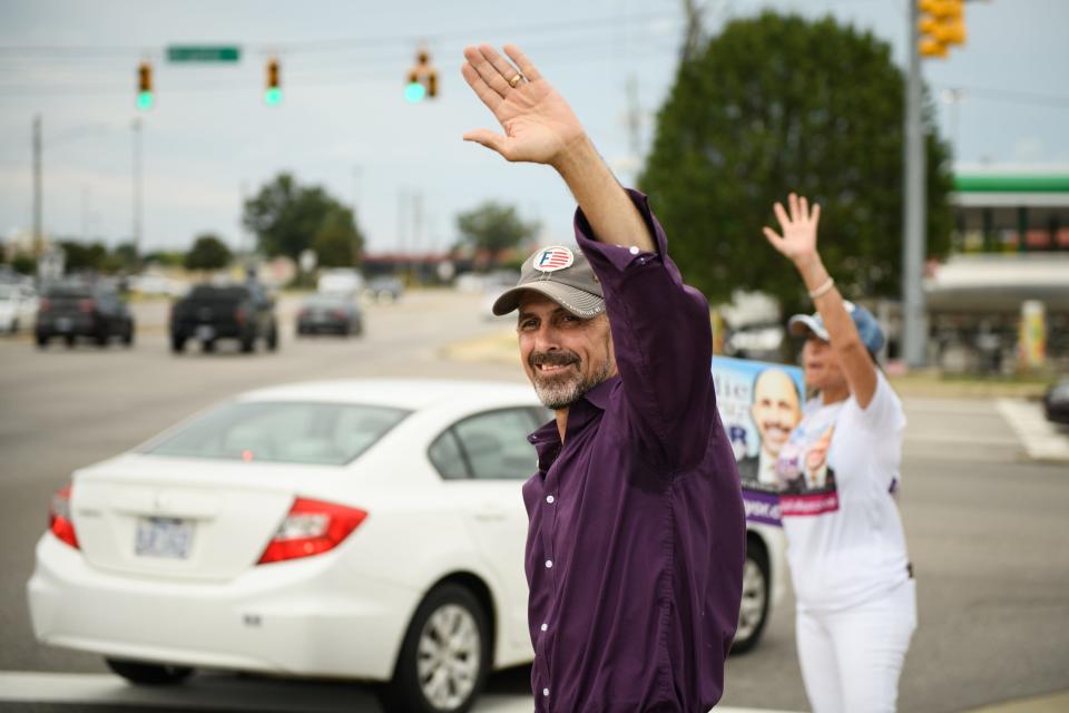 Mayoral candidate Freddie de la Cruz and his wife, Venus, wave to passing cars on Skibo Road on Tuesday, July 26, 2022.