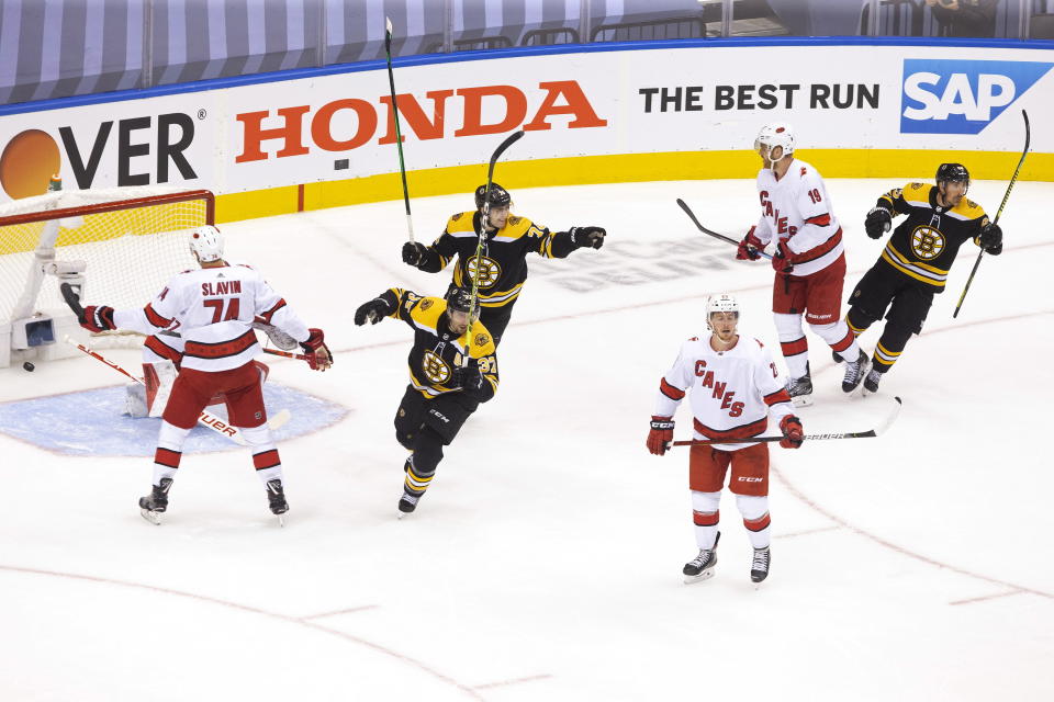 Carolina Hurricanes' Brock McGinn (23) Dougie Hamilton (19) and Jaccob Slavin (74) react as Boston Bruins' Patrice Bergeron (37), Jake DeBrusk (74) and Brad Marchand (63) celebrate David Krejci's goal during the first period of an NHL Eastern Conference Stanley Cup hockey playoff game in Toronto, Thursday, Aug. 13, 2020. (Chris Young/The Canadian Press via AP)