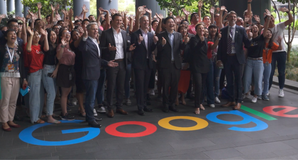Image showing Google senior executives and staff standing behind a Google logo painted on the floor. 