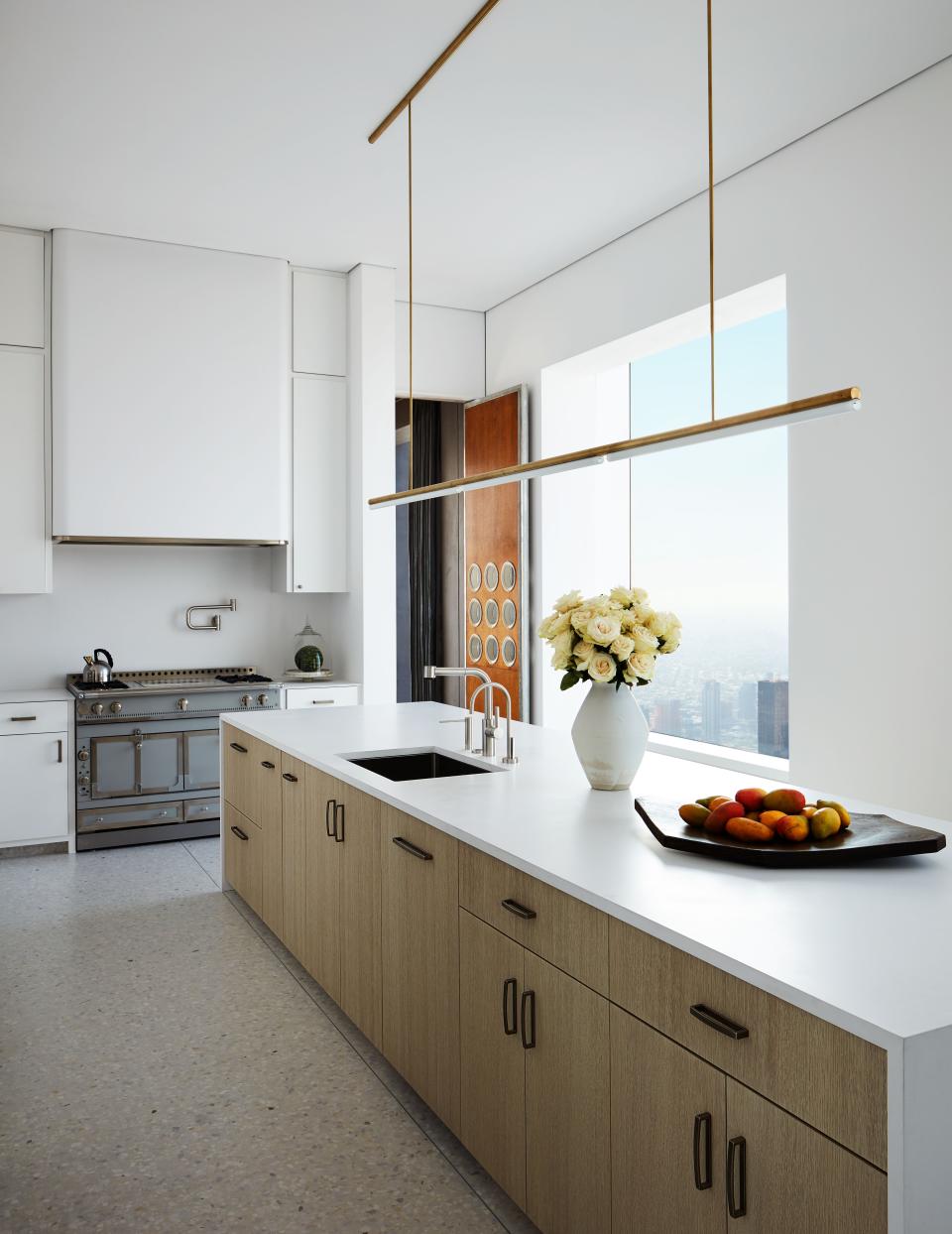 A Michael Anastassiades light hangs above a kitchen island with a Compac quartz countertop and cabinets of bleached and stained white oak. La Cornue range, Dornbracht fixtures, and H. Theophile pewter hardware.