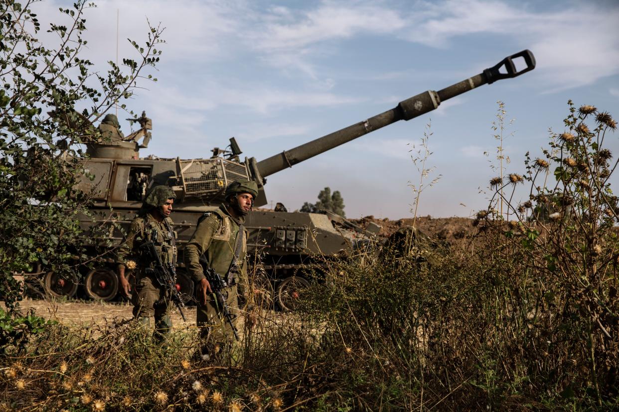 Two Israeli soldiers walk around an artillery unit, at the Israeli Gaza border, Sunday, May 16, 2021.