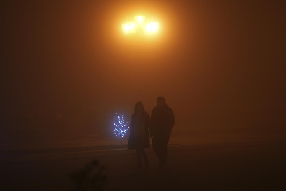 A couple walk in the fog along the street in a poorly lit Stepanakert, the capital of the separatist region of Nagorno-Karabakh, also known as Artsakh, on Thursday, Dec. 15, 2022. In the region have been periodic shutoffs of gas and electricity to the region during the dispute. Protesters claiming to be ecological activists have blocked the only road leading from Armenia to Nagorno-Karabakh for more than a month, leading to increasing food shortages. (Edgar Harutyunyan/PAN Photo via AP)