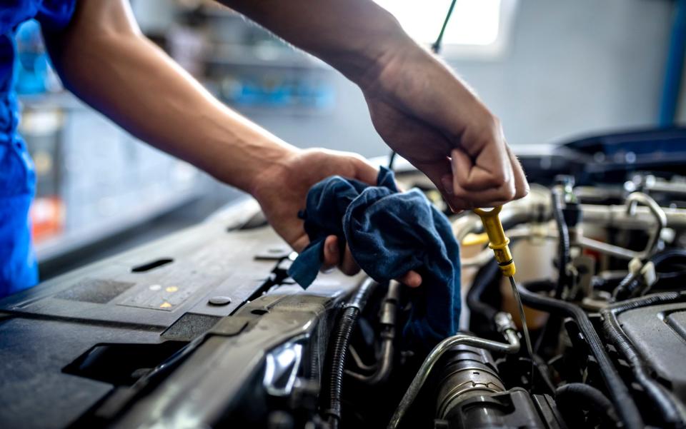 male mechanic measuring the oil level of a car engine - Ljubaphot/Getty Images