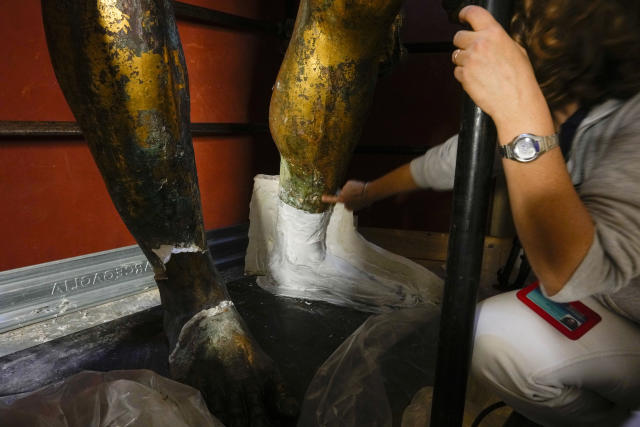 Vatican Museum restorer Alice Baltera points at a plaster cast on one of the feet of the bronze Hercules statue, in the Round Hall of the Vatican Museums, Thursday, May 11, 2023. Work will continue until December to reveal the 4-meter- (13-foot-) tall Hercules, believed to have stood in ancient Rome’s Pompey Theater, to its original golden sheen. The discovery of the gilded bronze in 1864 during work on a banker’s villa near Piazza dei Fiori made global headlines. (AP Photo/Andrew Medichini)