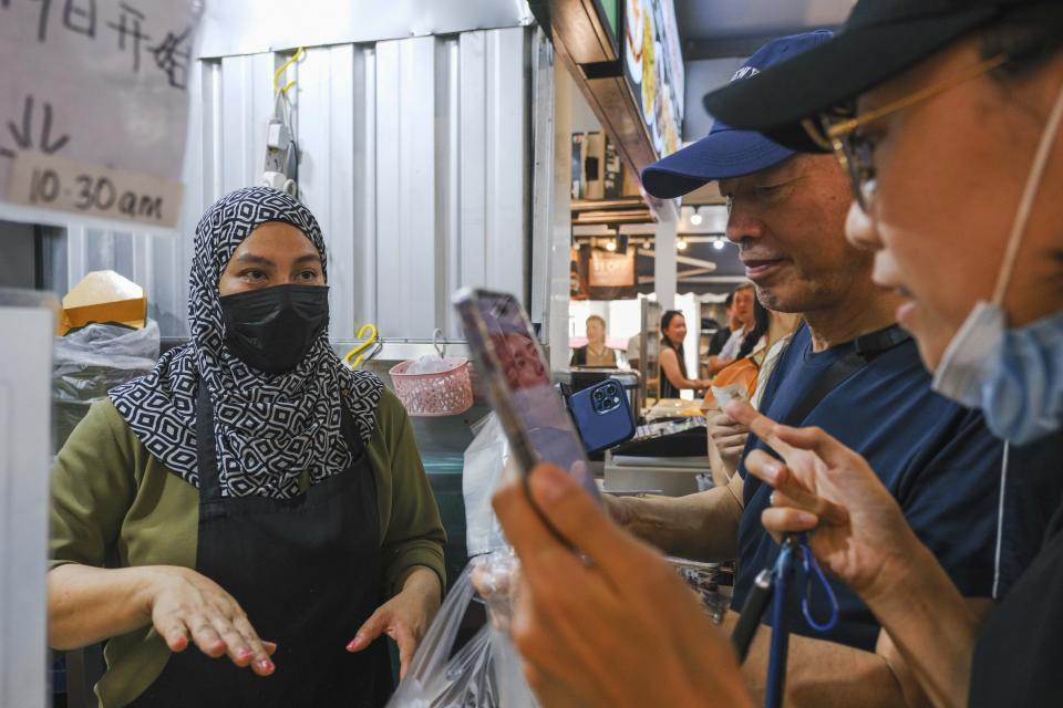 Aidah Rahim, wife of singaporean soccer goalkeeper Hassan Sunny, talks to Chinese customers at her food stall in Singapore, Friday, June 14, 2024. Chinese soccer fans have poured their love into Hassan's food stall after his performance in a game this week indirectly helped China advance to the third qualifying round for the World Cup in 2026. (AP Photo/Tim Chong)