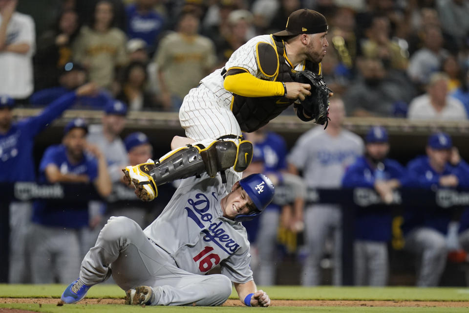 San Diego Padres catcher Victor Caratini leaps over Los Angeles Dodgers' Will Smith after tagging him out during the thirteenth inning of a baseball game Wednesday, Aug. 25, 2021, in San Diego. (AP Photo/Gregory Bull)