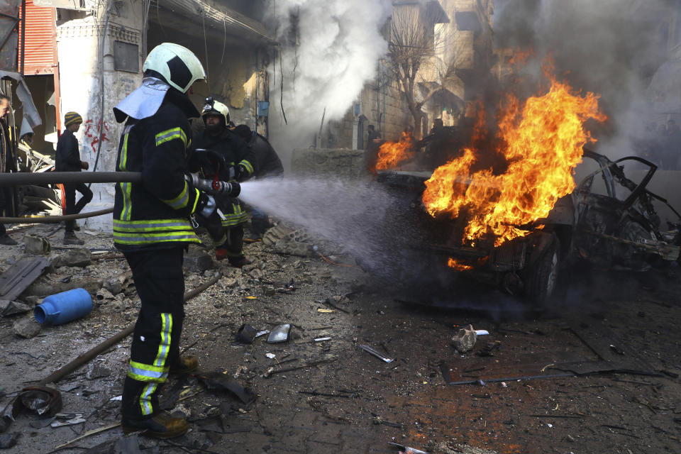 This photo provided by the Syrian Civil Defense White Helmets, which has been authenticated based on its contents and other AP reporting, shows a Syrian White Helmet civil defense worker, extinguishes flames rising from a burning car, in the town of Afrin, north of Aleppo, Thursday, Jan. 20, 2022. The rocket attack on Afrin, controlled by Turkey-backed opposition fighters, killed several civilians and wounded over a dozen people on Thursday, Syrian rescuers and a war monitor said. Both blamed U.S-backed Syrian Kurdish forces for the attack. (Syrian Civil Defense White Helmets via AP)