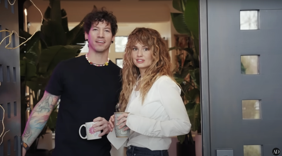 Josh and Debby smiling in their doorway, holding coffee mugs