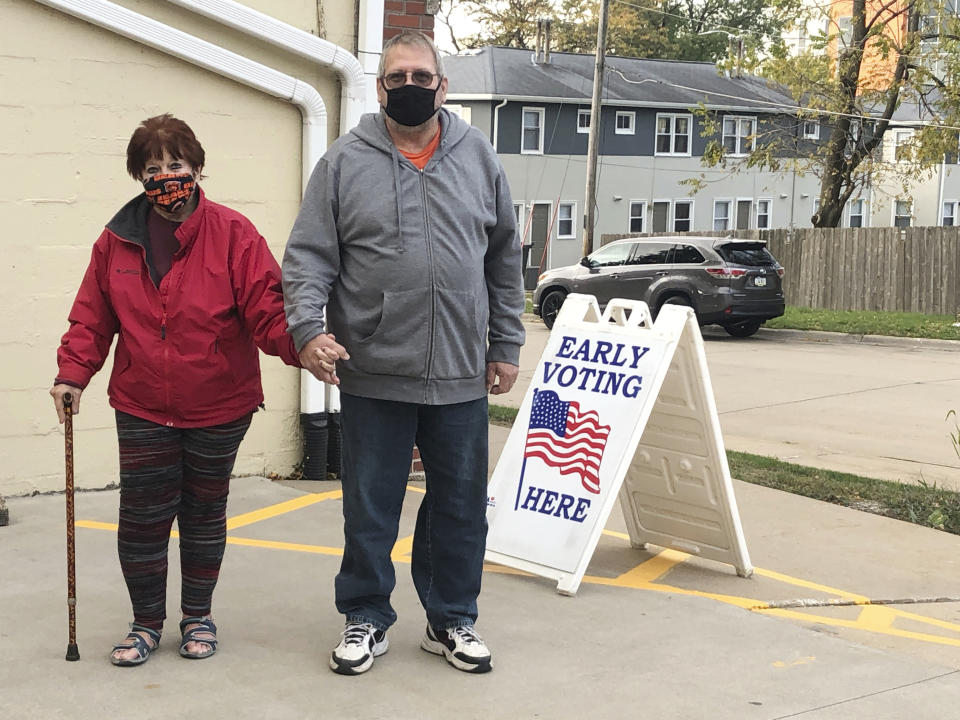 Tim and Pat Tompkins pause for a picture on their way to early vote in Bettendorf, Iowa, Friday, Oct. 16, 2020. Tompkins said he and his wife, Pat, were concerned about coronavirus exposure in bigger crowds and brought their own sanitizer, but were determined to vote. (AP Photo/Geoff Mulvihill)