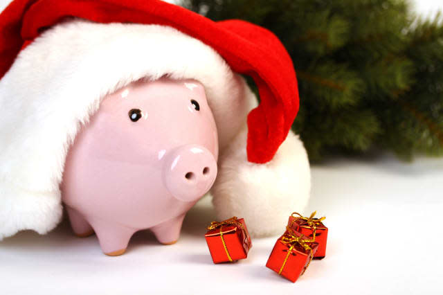 Part of piggy bank with Santa Claus hat and three little gifts and christmas tree standing on white background