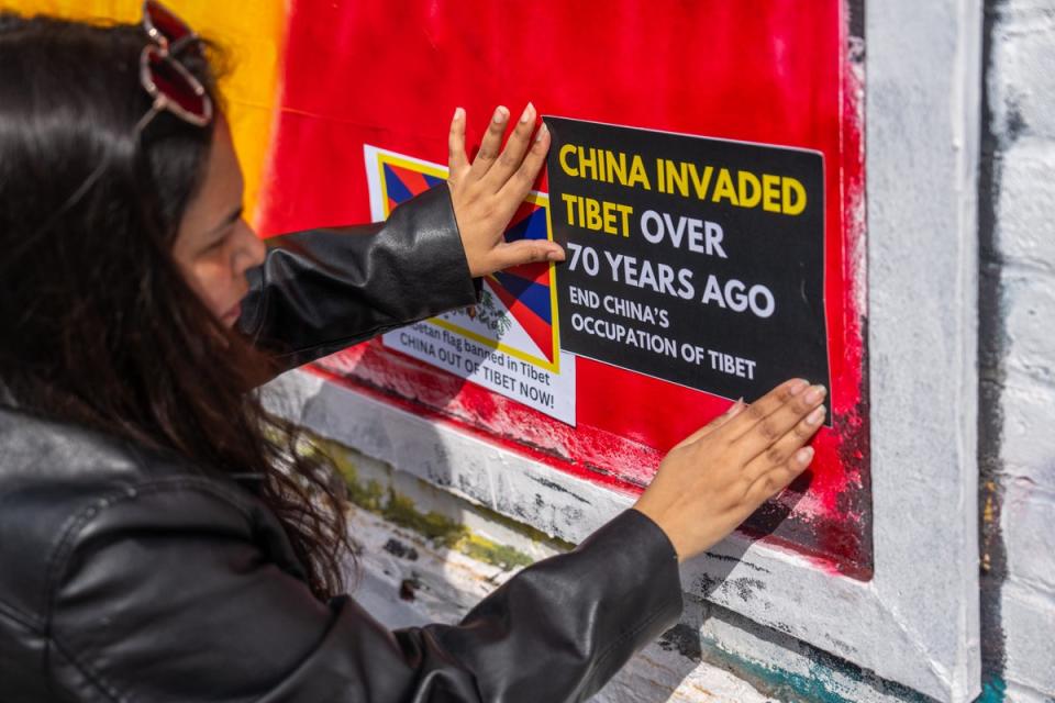 A woman sticks a Tibetan independence poster on an area of wall that had been graffitied with Chinese Communist Party ideology (Getty Images)