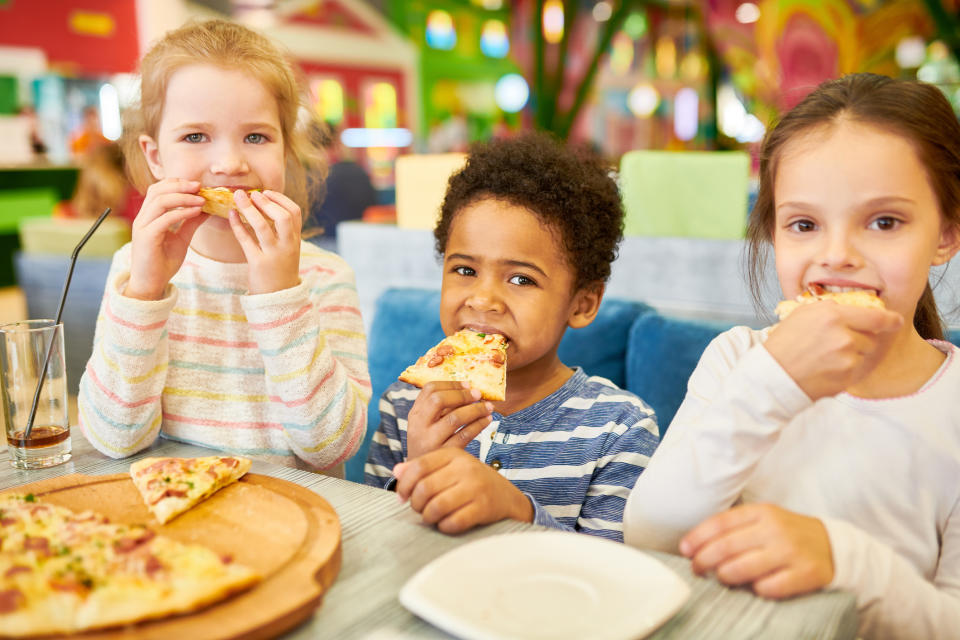 Three children sitting at a table, enjoying slices of pizza together