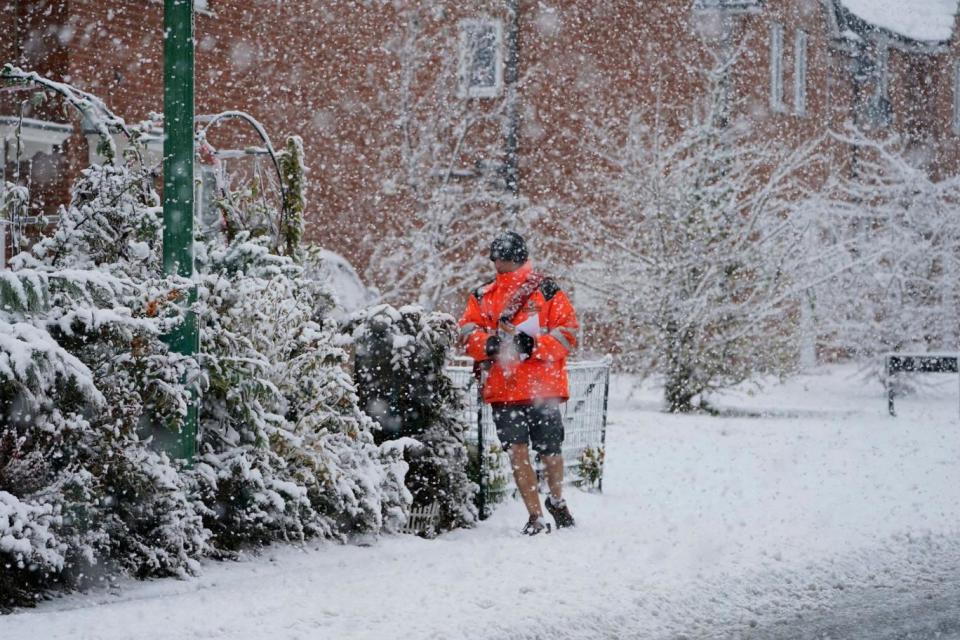 A postman in shorts delivers mail in the snow near Consett, County Durham (PA)