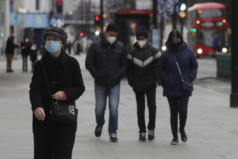 Pedestrians wear masks as they walk on Oxford Street in London, Saturday, Dec. 26, 2020. London is currently in Tier 4 with all non essential retail shops closed and people have been asked to stay at home, on what is usually one of the busiest retail days of the year with the traditional Boxing Day sales in shops. (AP Photo/Kirsty Wigglesworth)