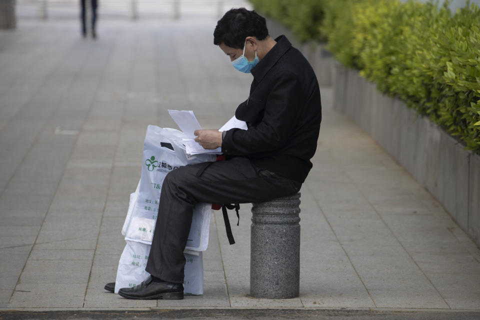 A man reads a medical report while holding CT scans between his legs near a hospital in Wuhan in central China's Hubei province Thursday, April 16, 2020. (AP Photo/Ng Han Guan)