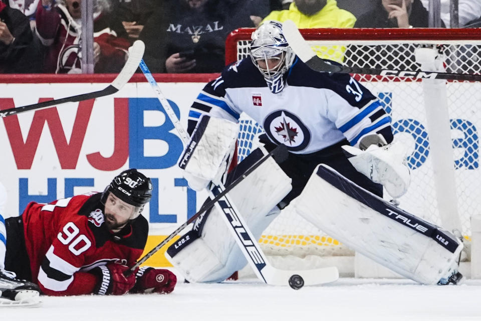 Winnipeg Jets goaltender Connor Hellebuyck (37) watches the puck, next to New Jersey Devils' Tomas Tatar (90) during the first period of an NHL hockey game Sunday, Feb. 19, 2023, in Newark, N.J. (AP Photo/Frank Franklin II)