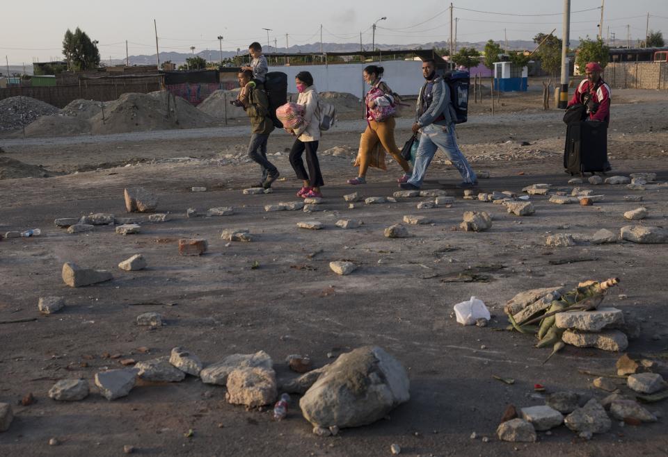 Venezuelan migrants heading to Chile walk around a blockade on the Pan-American South Highway set up by farmworkers on the fourth day of protests against the Agricultural Promotion Law, in Villacuri, Ica province, Peru, Thursday, Dec. 3, 2020. The farmworkers are asking for the elimination of the law, demanding better wages and health benefits. (AP Photo/Rodrigo Abd)