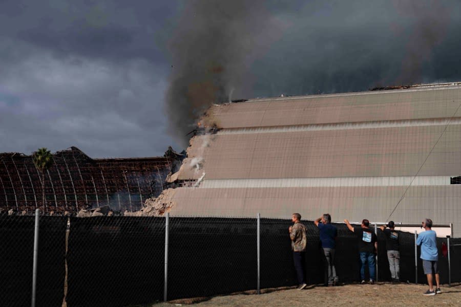 Spectators watch as a historic blimp hangar burns in Tustin, Calif., Tuesday, Nov. 7, 2023. A fire destroyed a massive World War II-era wooden hangar that was built to house military blimps based in Southern California. (AP Photo/Jae C. Hong)