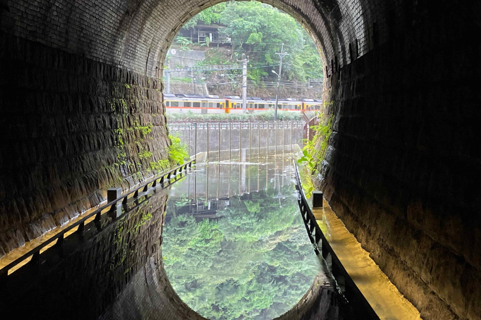 在三瓜子隧道設計的鏡面水池反射出翠綠山色及火車行經影像