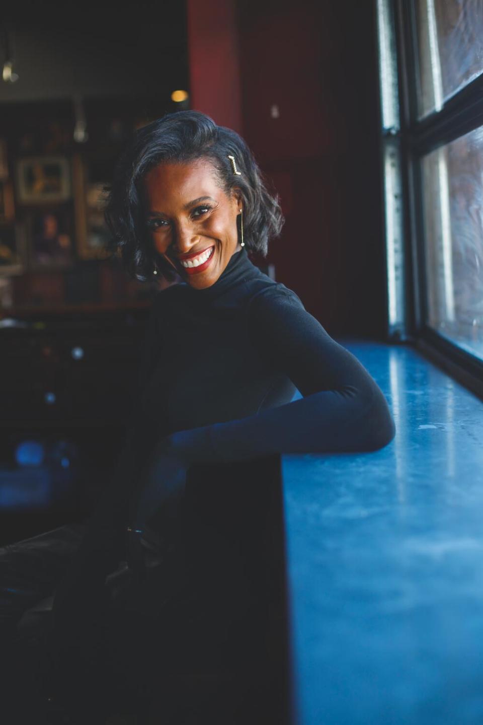 Woman in all black standing near the stage of the Improv next amongst a row of chairs