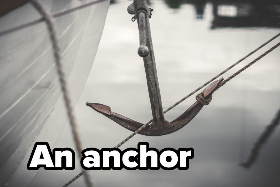 A close-up photo of a ship's anchor partially submerged in water, attached to thick ropes. The side of the boat is visible on the left