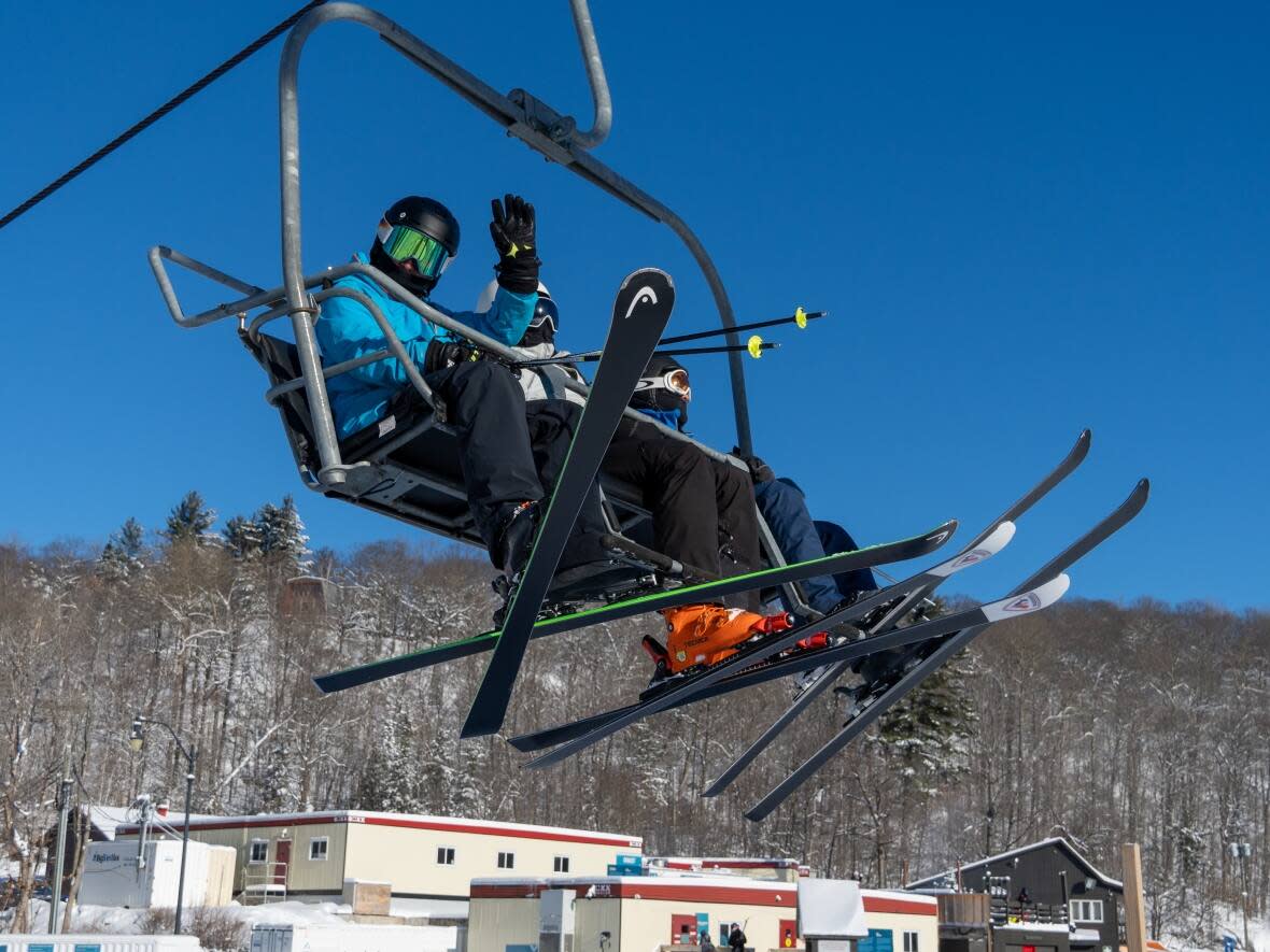 A skier waves from the chairlift at the Mont Cascades resort near Cantley, Que., on Jan. 14, 2023. A new report says Quebec ski resorts saw revenues bounce back last winter as pandemic restrictions lifted and tourists — especially Ontarians — flocked to the hills in droves. (David Bates-Taillefer/Radio-Canada - image credit)