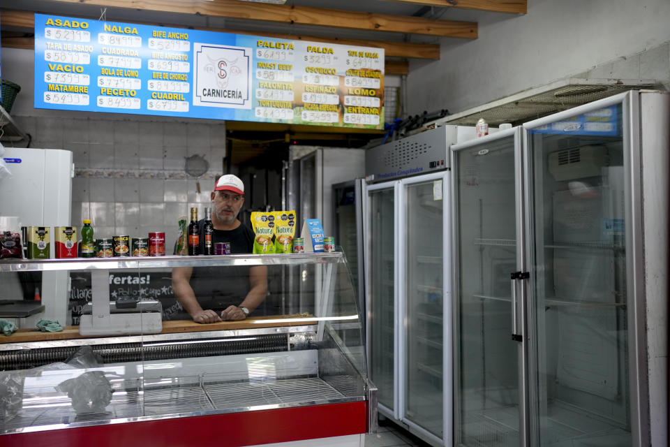 Sergio Gómez stands behind an empty meat display case inside his butcher shop, in Buenos Aires, Argentina, Wednesday, March 6, 2024. Above him is a blackboard displaying outdated prices for the different cuts that he no longer sells. (AP Photo/Natacha Pisarenko)