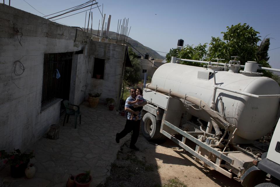 In this April 17, 2014 photo, a Palestinian landlord carries his daughter by a sewage tank vehicle that he rents to vacuum his house's underground wastewater storage container, at the Palestinian village of Silwad, adjacent to the Israeli settlement of Ofra, north of the West Bank city of Ramallah. (AP Photo/Nasser Nasser)