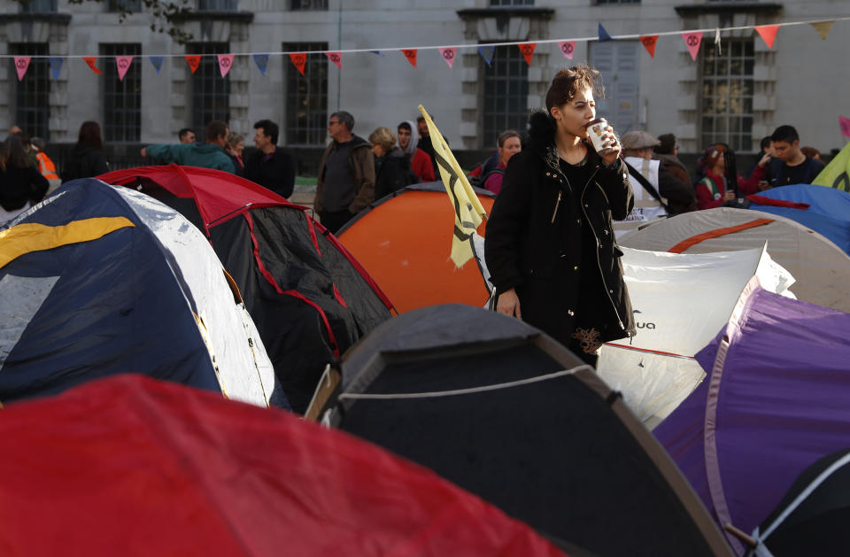 A Climate change protester sips her drink after getting out of her tent on Whitehall in London, Tuesday, Oct. 8, 2019. Some protesters have set up a tented village, disrupting the usual traffic in central London. Police are reporting they have arrested more than 300 people at the start of two weeks of protests as the Extinction Rebellion group attempts to draw attention to global warming .(AP Photo/Alastair Grant)