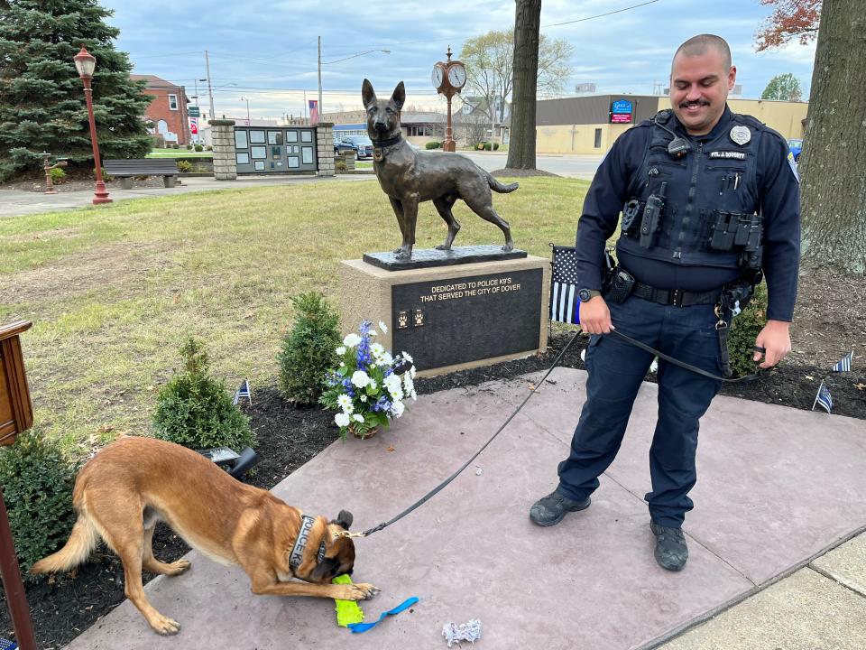 Dover K-9 Red plays with a toy Saturday in front of the city's new K-9 monument as his handler, Officer Jordan Doughty, watches.